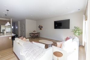 Ein modernes Wohnzimmer mit einer Couch, einem Esstisch mit Stühlen, einer Küchenzeile und einem flachbildfernseher an der Wand.