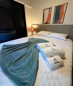 Habitación de hotel con cama, almohadas, manta, lámpara y dos cuadros abstractos en la pared.