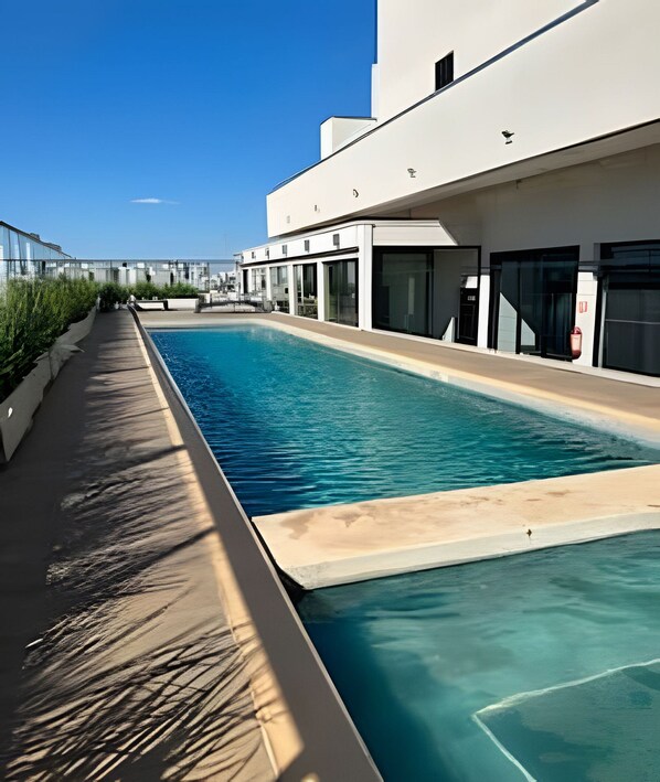 Una piscina junto a un edificio con amplios ventanales y cielo despejado.