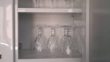 Un mueble blanco con estantes que contienen copas de vino, botelleros de cristal y tazas blancas.