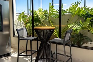 Una habitación pequeña y moderna con dos sillas, una mesa, ventanas amplias y plantas de interior.