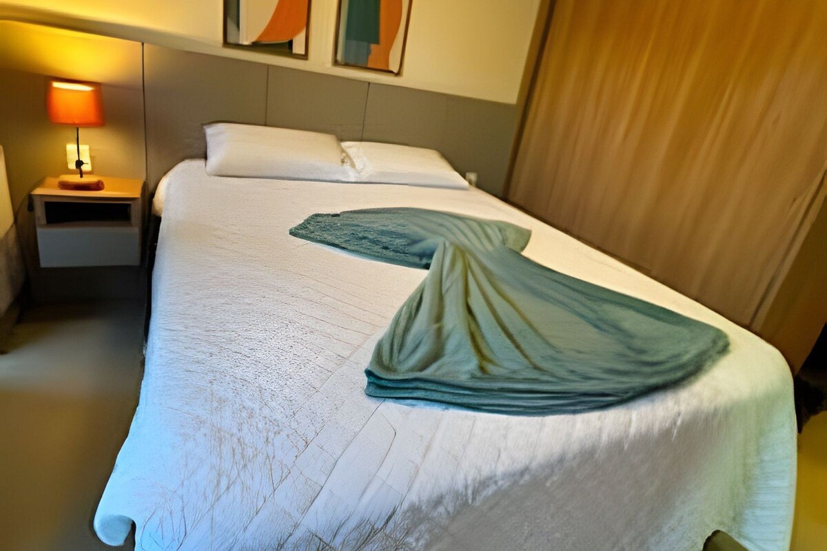 Una habitación de hotel con una cama, una mesita de noche, una lámpara y dos cuadros abstractos en la pared.