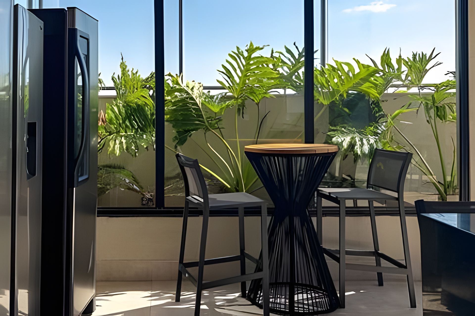 Un balcón con mesa y sillas, un televisor y vistas a plantas verdes.