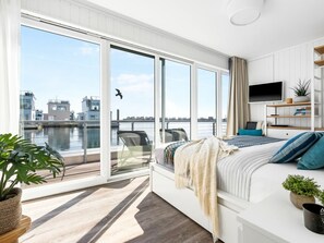 Ein modernes Schlafzimmer mit einer großen Schiebetür zu einem Balkon, einem Bett mit Blick auf die Stadt und einem an der Wand montierten Fernseher.