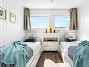 Une chambre avec deux lits, une table de chevet, une commode et une fenêtre avec des rideaux.