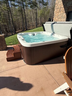 Ein Whirlpool mit Steinwand, Holzterrasse und einer von Bäumen gesäumten Grünfläche.