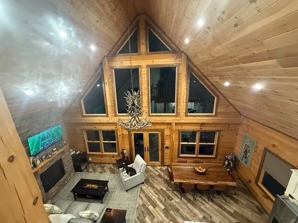 A high-ceilinged wooden interior with a fireplace, seating area, and large windows.