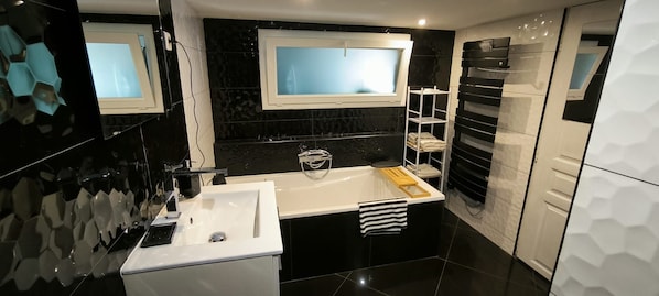 Un baño moderno con un lavamanos blanco, una bañera y una ventana sobre el espejo.