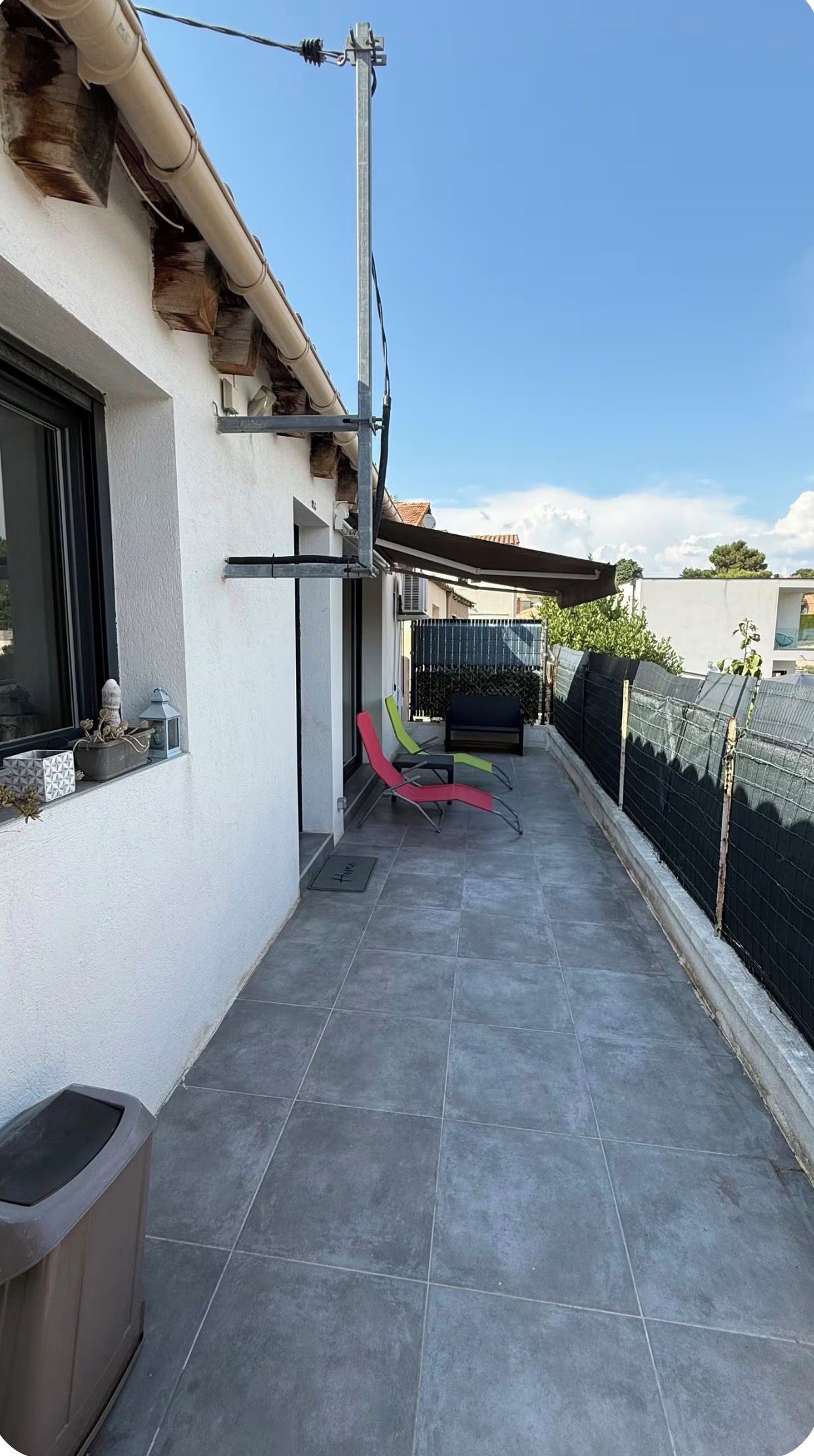 A narrow outdoor balcony with a tiled floor, a metal railing, and a black fence.