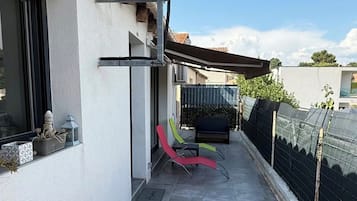 A narrow outdoor balcony with a tiled floor, a metal railing, and a black fence.