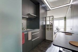 A modern kitchen with grey cabinets, a stainless steel range hood, a countertop with a sink, and a dining area with a table and chairs. - 77 - Le Lokup - Wifi - Proche tram (Reims)