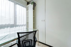 A room with a glass table and black mesh chair, white walls, and a plant on the wall. - 02 - Le Lokup - Wifi - Proche tram (Reims)