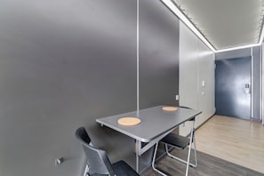 Ein moderner Konferenzraum mit einem metallischen Tisch und Stühlen, einem Holzboden und einer Tür im Hintergrund.