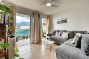 Ein Wohnzimmer mit grauem Sofa, einem kleinen Tisch und einem Balkon mit Topfpflanzen.