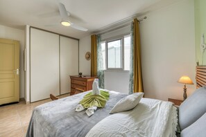 Ein Schlafzimmer mit einem Bett, einem Deckenventilator, einem Fenster mit Vorhängen, einer Nachttischlampe und einer Tür.