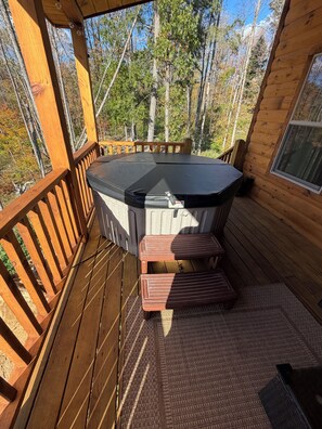 A wooden deck with a hot tub, wooden benches, and a view of trees. - New 3-bedroom cabin in ADK with hot tub (Wells)