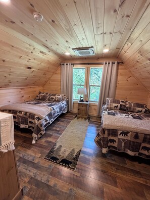 A cabin-style room with two beds, a small table, and a window with curtains. - New 3-bedroom cabin in ADK with hot tub (Wells)