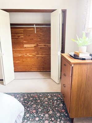 A bedroom with a wooden wardrobe, a bed with a floral bedspread, and a small potted plant on a dresser. - Hillside Haven Cozy 2BR Near Pullman and WSU (Colfax)