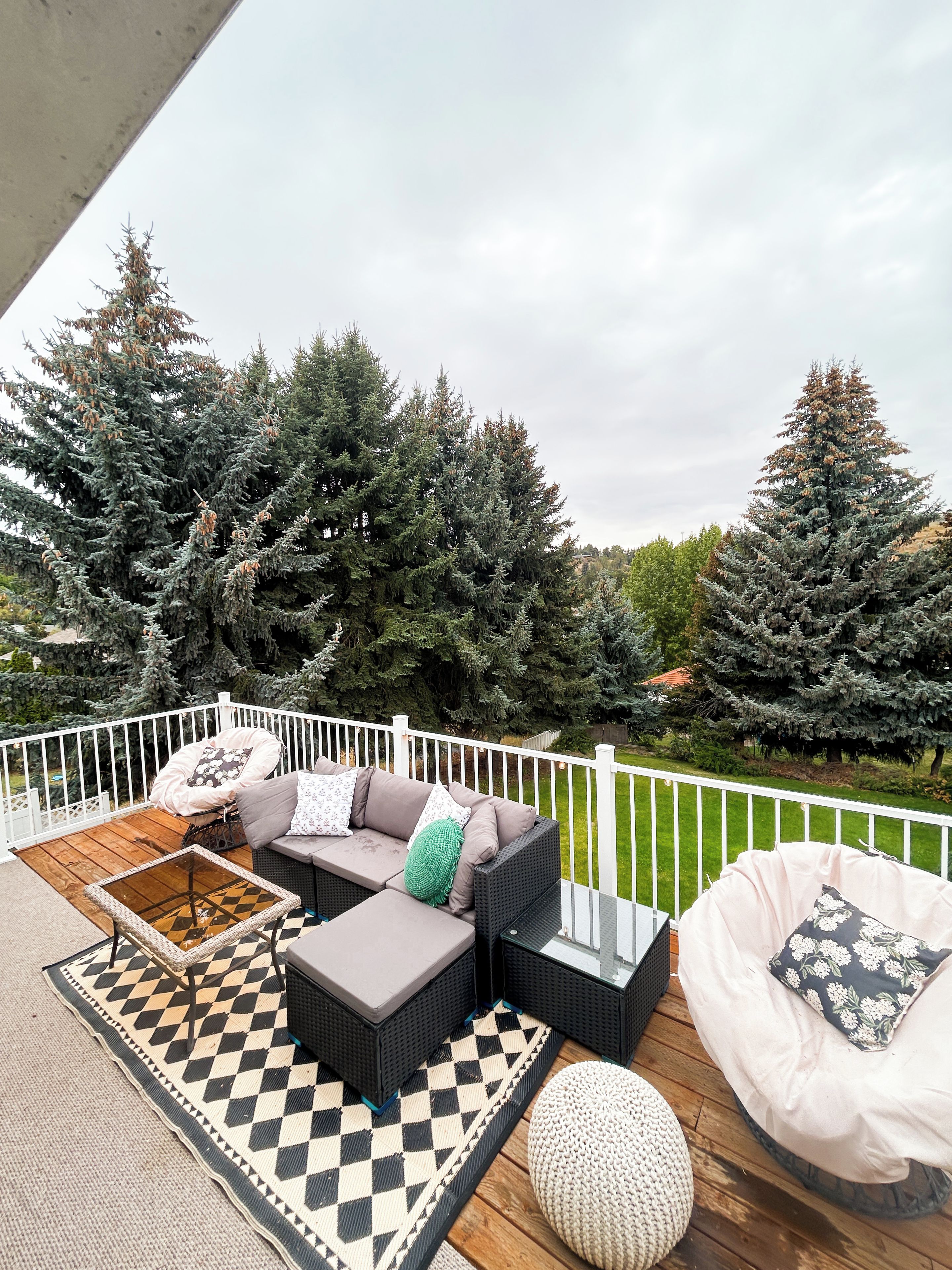 A deck with outdoor furniture, including a sofa and chairs, and a checkered rug.