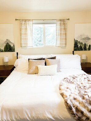 A neatly made bed with white linens and multiple pillows, a window with plaid curtains, and two wall-mounted lamps. - Hillside Haven Cozy 2BR Near Pullman and WSU (Colfax)