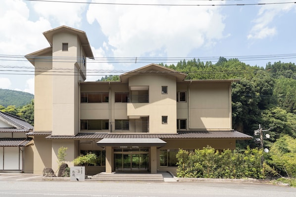 A two-story hotel with a flat roof, a covered entrance, and a sign indicating it is the Onsen Hotel. - OKU-AMAGASE ONSEN OHANA (Hita)