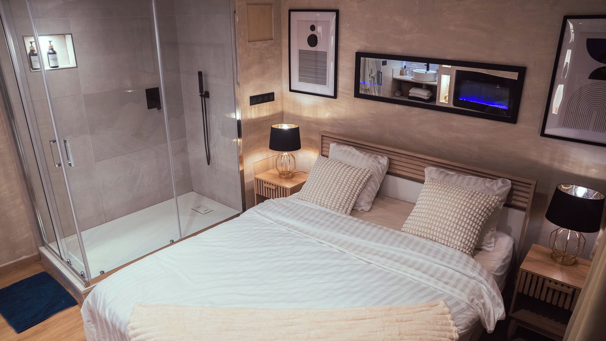 A hotel room with a bed, bedside tables, a nightstand, a shower area, and a mirror.