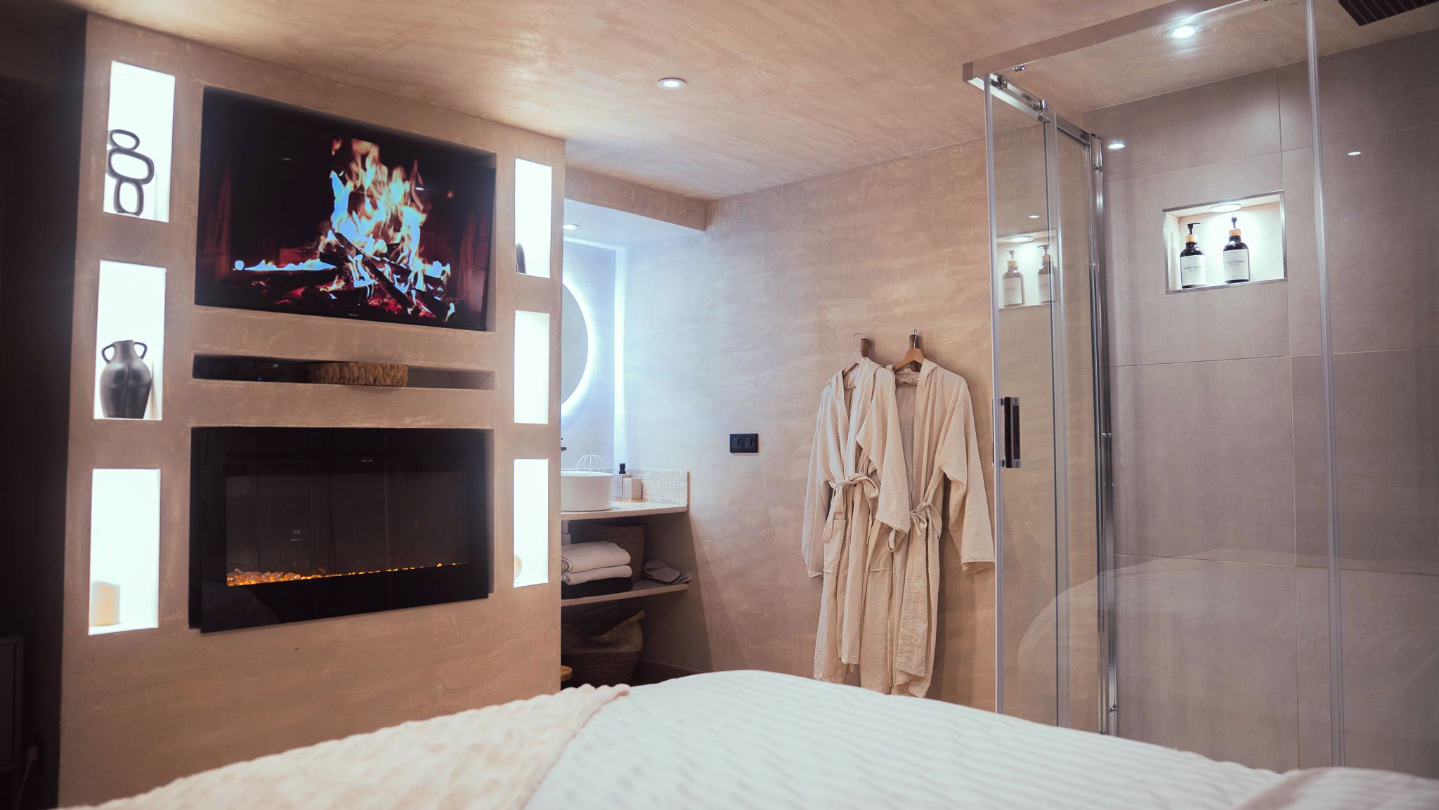 Une chambre d’hôtel moderne équipée d’un lit, d’un téléviseur fixé au mur, d’une douche en verre et d’un peignoir accroché au mur.