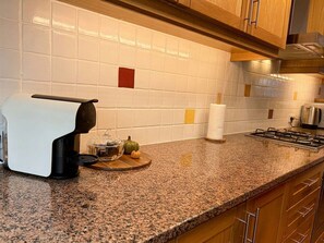 Eine Küche mit Kaffeemaschine, Papierhandtuchhalter, Gaskochfeld und einer kleinen Kürbis auf einem Schneidebrett.