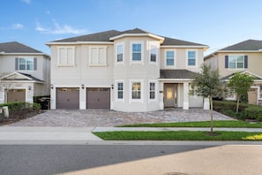 A two-story residential building with a symmetrical facade, a central entrance with a door, and a garage. - 11br Near Disney Pool, spa & Home Theater (Kissimmee)