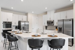 A modern kitchen with white cabinetry, stainless steel appliances, and a central island with bar stools. - 11br Near Disney Pool, spa & Home Theater (Kissimmee)