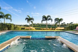 A swimming pool with a hot tub in the center, surrounded by palm trees and a grassy area. - 11br Near Disney Pool, spa & Home Theater (Kissimmee)