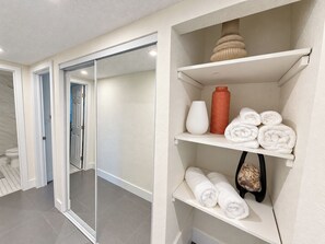 Et badeværelse på et hotel med bruser, håndklædestativ med håndklæder, en vase og en flaske.
