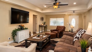 A living room with a flat-screen TV, leather sofas, a coffee table, and a ceiling fan. - Relax, Recharge & Play at 3-bedroom Bluewater Bungalow (Lake Havasu City)