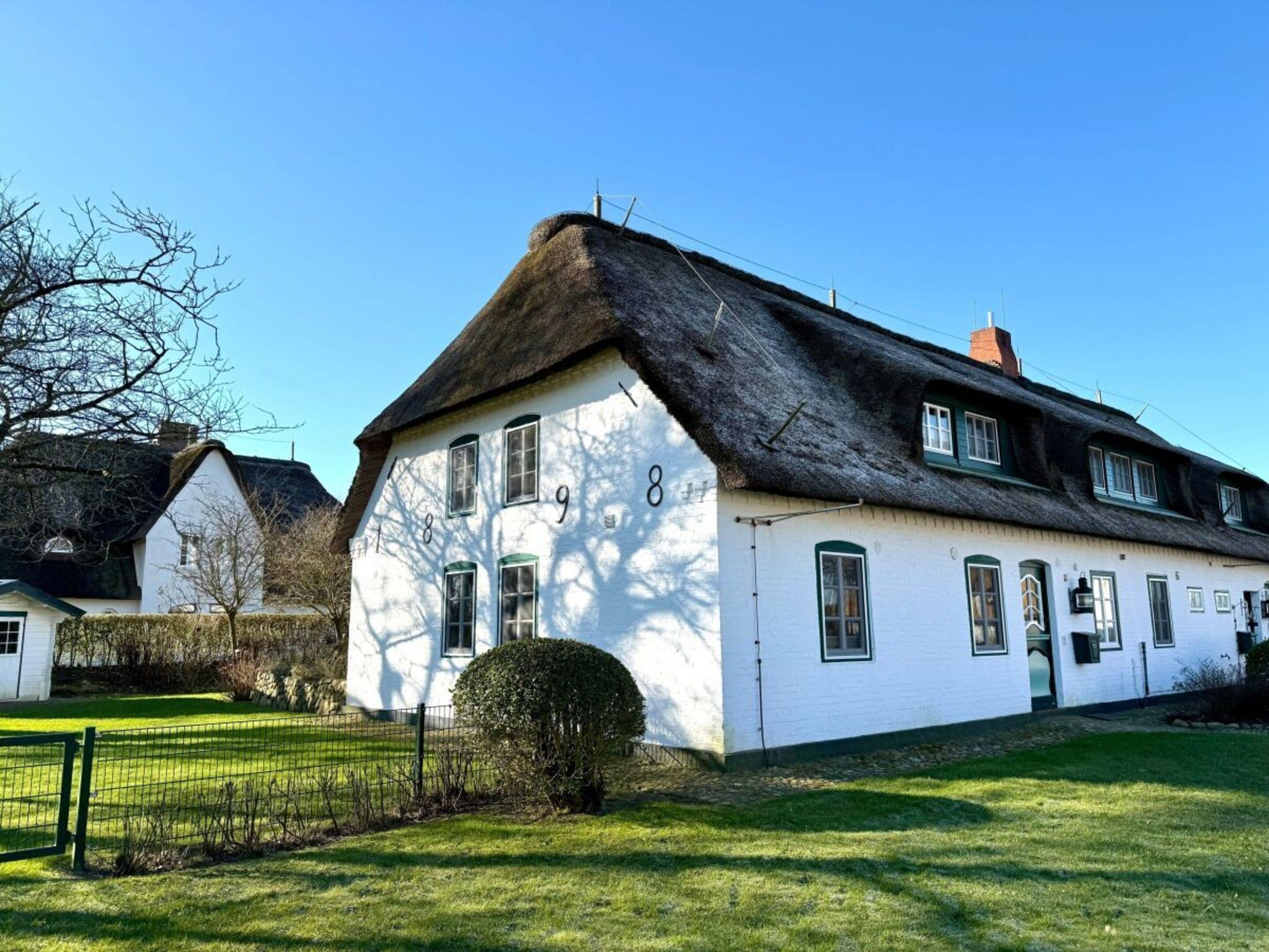 A white building with a thatched roof, numbered 8, and a small garden in front.