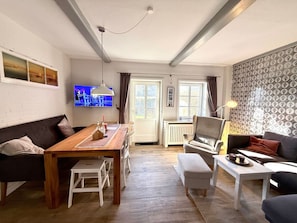 Ein Wohnzimmer mit einer Couch, einem Esstisch und einem an der Wand befestigten Fernseher.