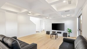 A modern living room with a flat-screen TV, black leather sofas, wooden flooring, and a staircase leading to another level. - The Gathering House – Spacious Island Retreat (Cowes)