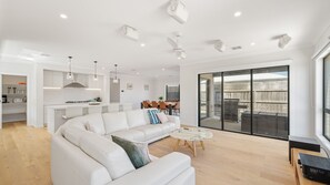 A modern living room with a white sectional sofa, a round coffee table, and a dining area with a wooden table and chairs. - The Gathering House – Spacious Island Retreat (Cowes)