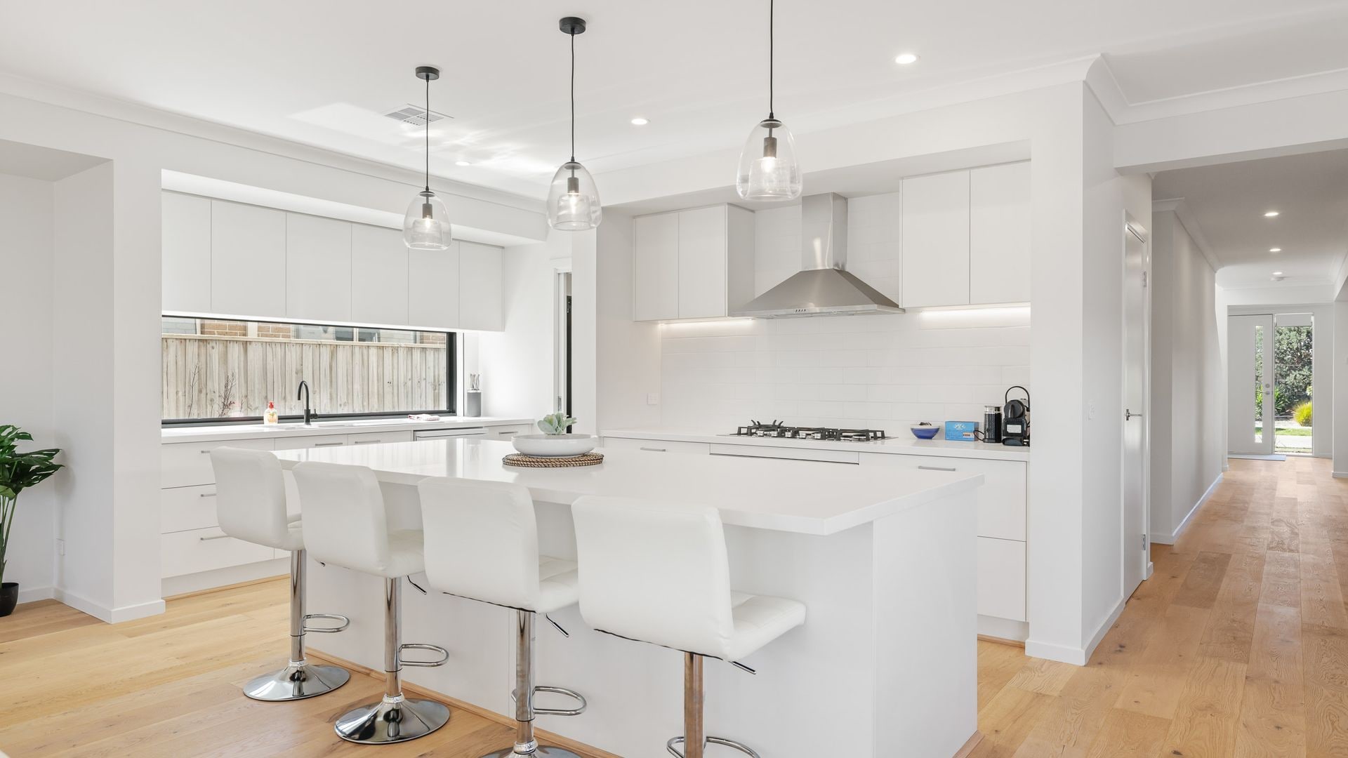 A modern kitchen with white cabinetry, a central island with bar stools, pendant lighting, and a view to the outside.