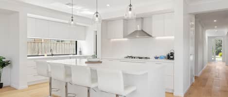 A modern kitchen with white cabinetry, a central island with bar stools, pendant lighting, and a view to the outside.