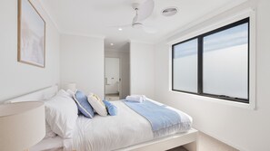 A bedroom with a bed, a ceiling fan, a window, and a door leading to a bathroom. - The Gathering House – Spacious Island Retreat (Cowes)