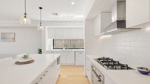 A modern kitchen with white cabinetry, a central island, stainless steel appliances, and pendant lighting. - The Gathering House – Spacious Island Retreat (Cowes)