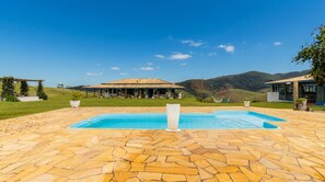 Ein Poolbereich mit einer Steinterrasse, einer überdachten Sitzgelegenheit und Blick auf die umliegende Landschaft.