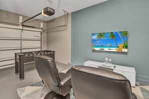 Ein Zimmer mit einem Tischkicker, einem an der Wand befestigten Fernseher und einem Strandbild.