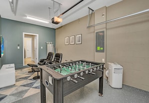 Ein Zimmer mit einem Tischkicker, einem Sofa, einem Sessel, einem Fernseher und einem an der Wand befestigten Luftreiniger.