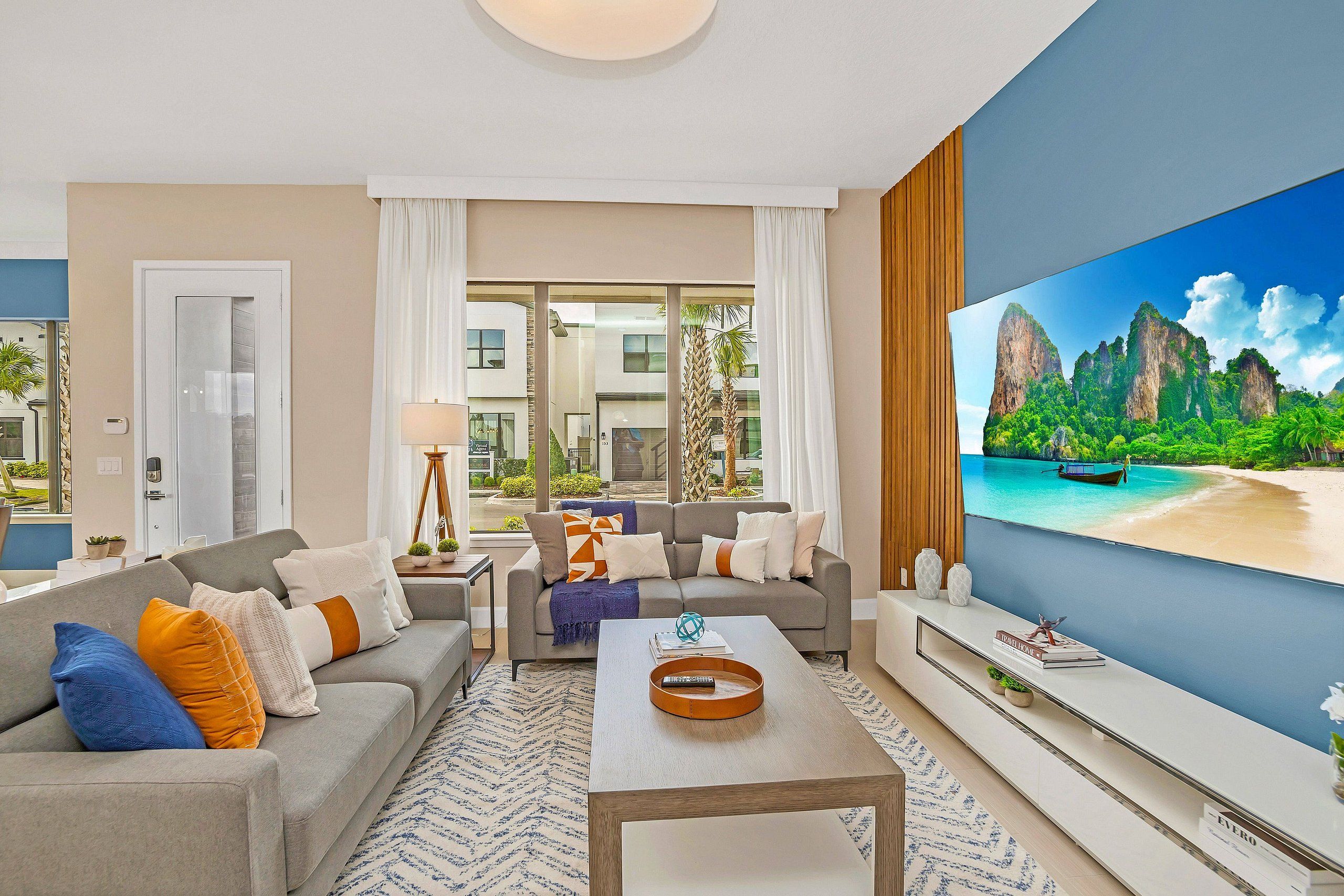 A modern living room with a large flat-screen TV, a sofa, a coffee table, and a view of a tropical landscape.