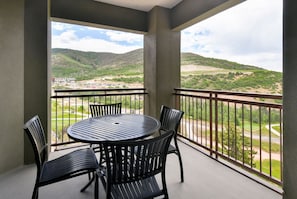 A balcony with a round table and four chairs, overlooking a hilly landscape with a parking area in the background. - 1 Bedroom Condo w/ Ski-in/out Access + Fireplace (Park City)