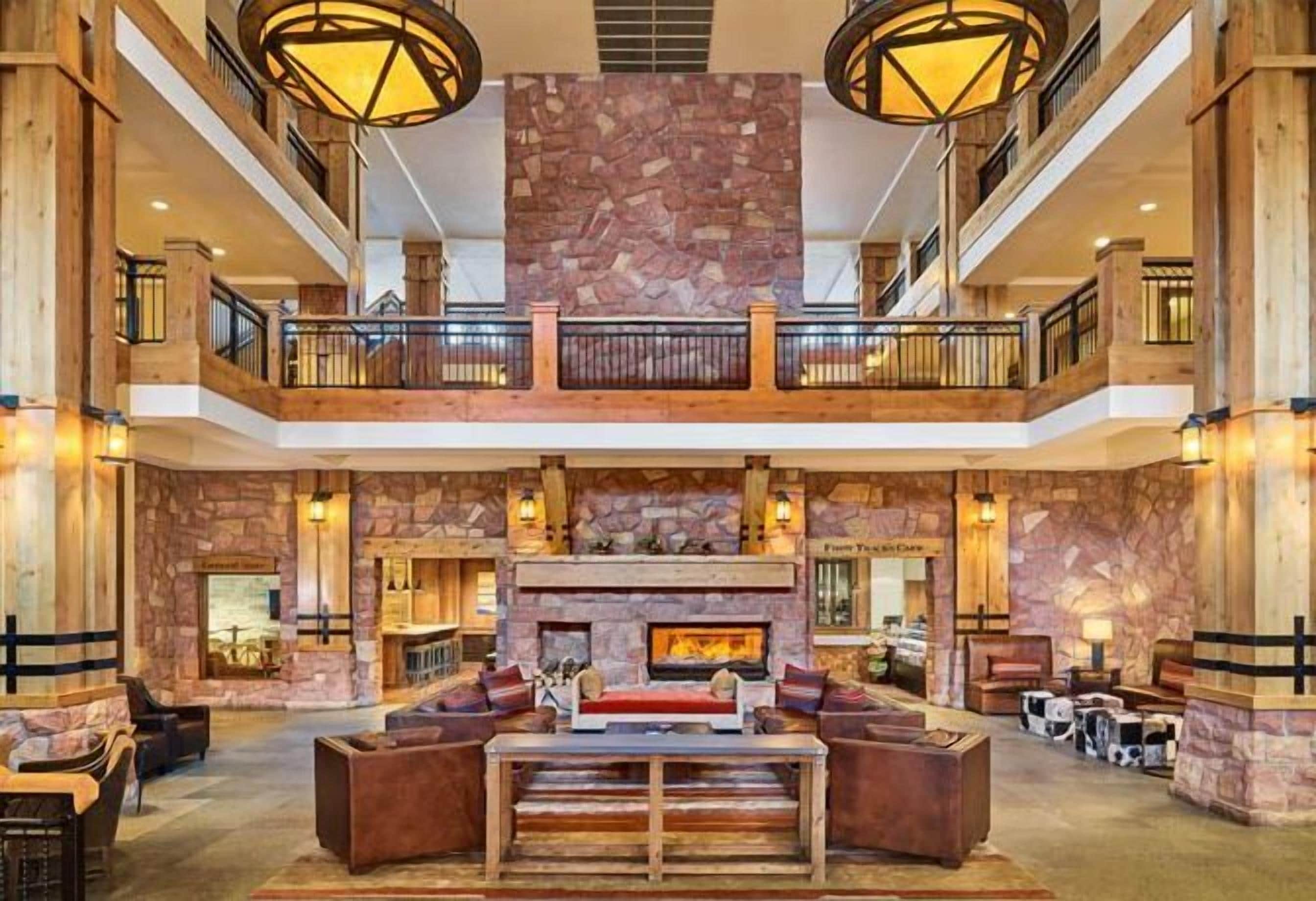 A spacious lobby with a central fireplace, a wooden reception desk, and a balcony with a stone wall backdrop.