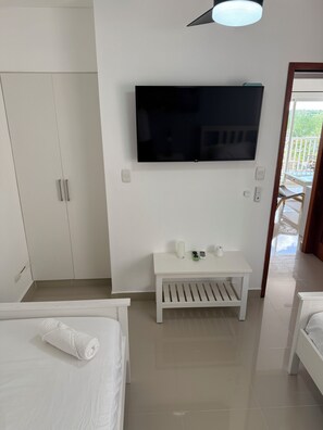 A hotel room with a bed, a TV mounted on the wall, a small table with a remote control, and a door leading to an outdoor balcony. - 2-bedroom apartment in marvelous Punta Cana with cool AC (Punta Cana)