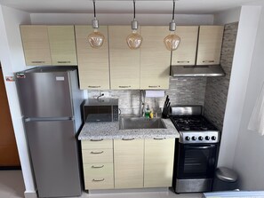 A compact kitchen with a stainless steel refrigerator, a microwave, a gas stove, and light wooden cabinets. - 2-bedroom apartment in marvelous Punta Cana with cool AC (Punta Cana)