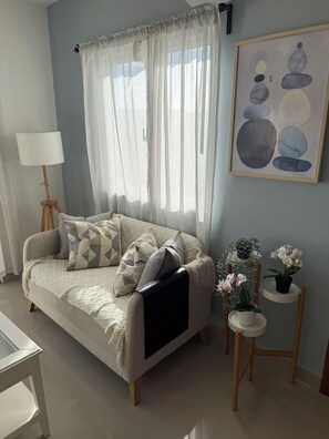 Een moderne woonkamer met een bank, een vloerlamp, een schilderij en een bijzettafeltje met plantenpotjes.